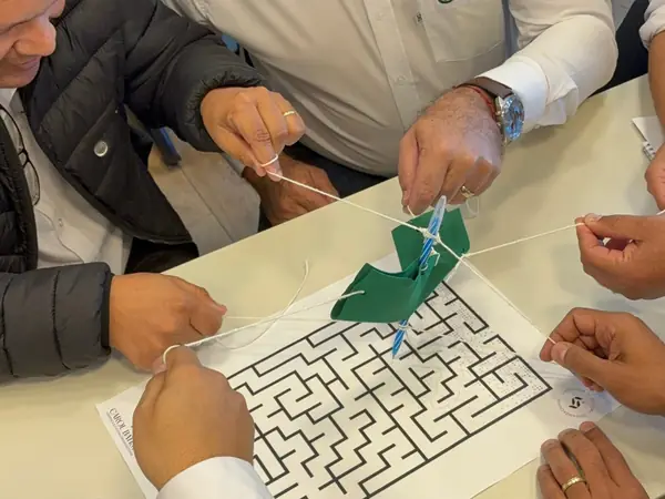 Mãos de participantes conduzindo cordas sobre um labirinto em dinâmica de equipe