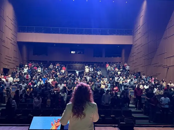 Carol de costas no palco, diante de um teatro lotado